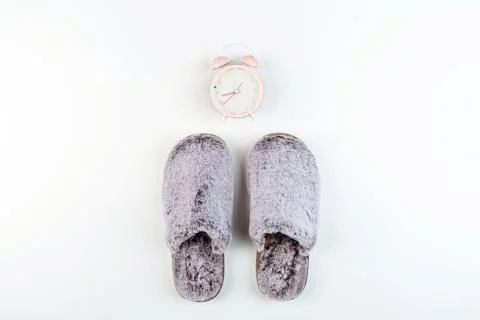 Flat lay with Soft fluffy slippers gray color and pink alarm clock isolated o Stock Photos