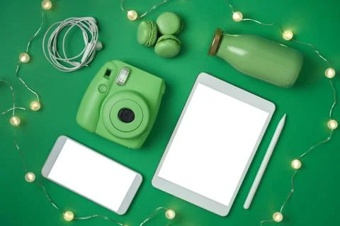 Flat lay tablet, phone, camera and headphones, bottle and macaroons on green Stock Photos