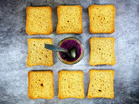 Flat lay of teaspoon dipped in a jar of grape jelly with rusks around Stock Photos
