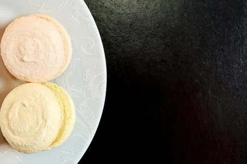 Flat lay template with tasty macaroons on the plate lays on the black surface Stock Photos
