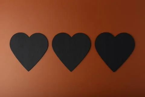 Flat lay with three black hearts on brown background. Concept of love and Stock Photos