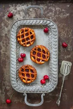 Flat lay of three individual cherry pies and fresh cherries on a serving tray 写真素材