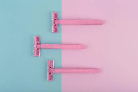 Flat lay with three pink razors on pink and blue background Stock Photos