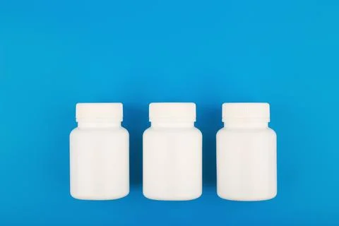 Flat lay with three white medication bottles in a row on blue background with Stock Photos
