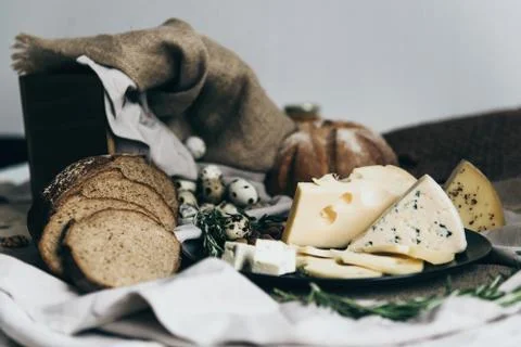 A flat lay of tiny eggs with baked bread on stylish tablecloth. A cup of milk is Stock Photos