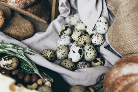 A flat lay of tiny eggs with baked bread on stylish tablecloth. A cup of milk is Stock Photos
