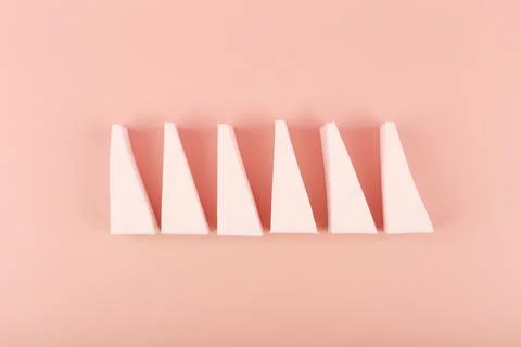 Flat lay with triangle shaped make up sponges in a row on pastel pink background Stock Photos