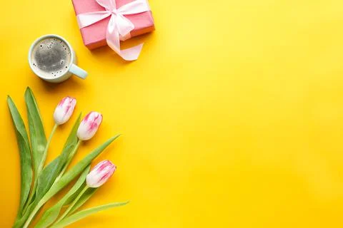Flat lay tulips, gift box and coffee on a yellow background, space for text. Stock Photos