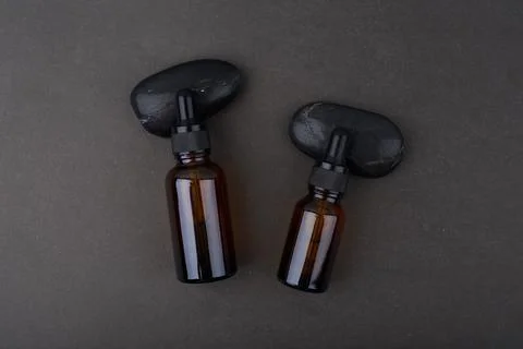Flat lay with two glass bottles with dropper on black background with stones Stock Photos