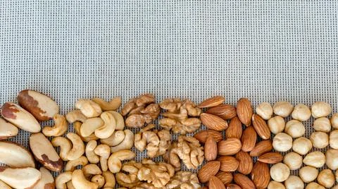 Flat lay with various nuts with copy space on grey fabric background Stock Photos