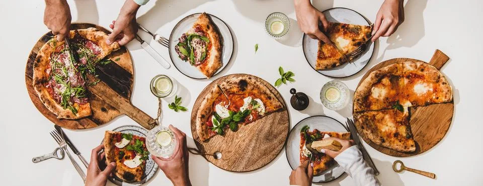 Flat-lay of various pizzas, drinks and peoples hands eating pizza Stock Photos