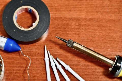 Flat lay of various soldering tools, rosin flux, and multimeter probes on a Foto stock