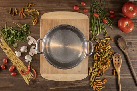 Flat lay of vegetables and pasta and a chopping board with a cacerola Stock Photos