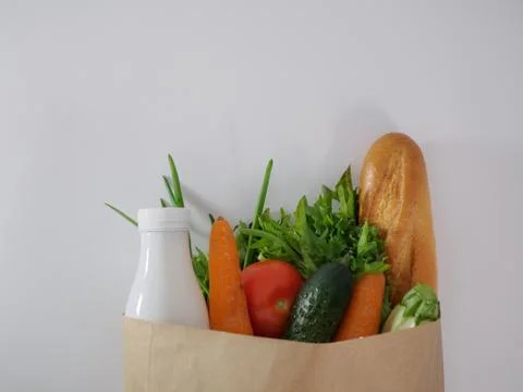 Flat lay of vegetables, herbs, bread and milk in a paper bag on a white Stock Photos