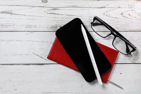 Flat lay view of a red notebook, smartphone, pen and black glasses on a white Stock Photos