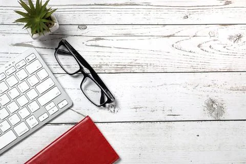 Flat lay view of a red notebook, white keyboard, pen and black glasses on a w Stock Photos