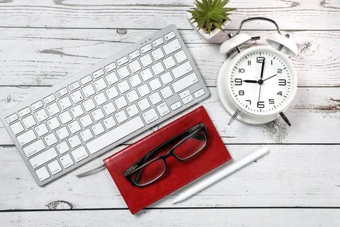 Flat lay view of a red notebook, white keyboard, pen and black glasses on a w Stock Photos