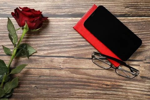 Flat lay view of a red notebook, red rose, smartphone, pen on a wooden backgr Stock Photos