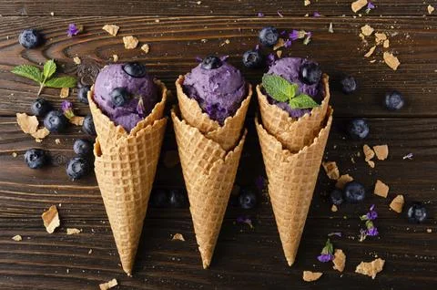 Flat lay view at wafer cones with blackberry icecream on wooden kitchen table Stock Photos