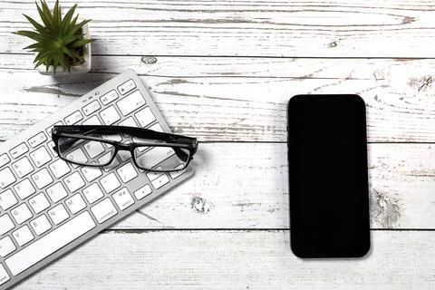 Flat lay view of white keyboard, smartphone and black glasses on a white wood Stock Photos