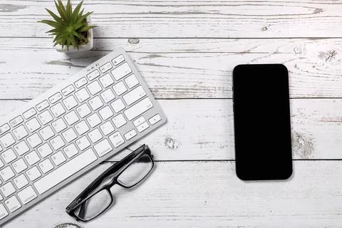 Flat lay view of white keyboard, smartphone and black glasses on a white wooden Stock Photos