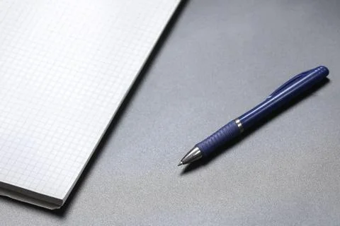 Flat lay view of a white notebook and blue pen on a black table. Copy space. Stock Photos