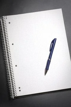 Flat lay view of a white notebook and blue pen on a black table. Copy space. Stock Photos