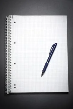 Flat lay view of a white notebook and blue pen on a black table. Copy space. Stock Photos