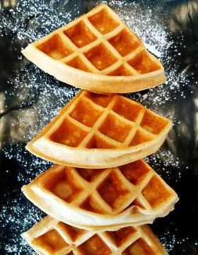 Flat lay of waffles with icing sugar on black plate at cafe shop. Stock Photos