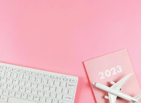 Flat lay of white computer keyboard, pink diary 2023 and airplane model  on.. Stock Photos