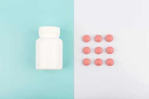 Flat lay with white glossy medication bottle and red round pills on blue and Stock Photos