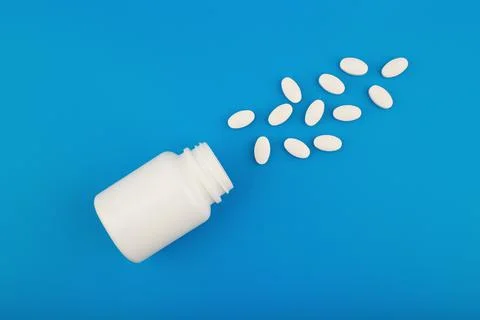 Flat lay with white medication bottle with spilled pills on blue background Stock Photos