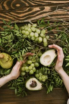 Flat lay of woman's hands holding grapes, pears and avocados with pistachio b Stock Photos