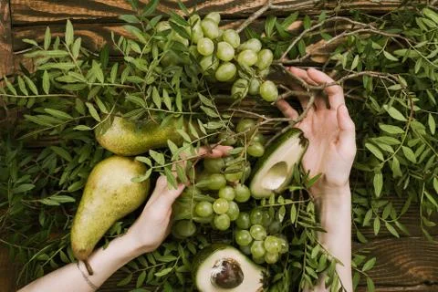 Flat lay of woman's hands holding grapes, pears and avocados with pistachio b Stock Photos