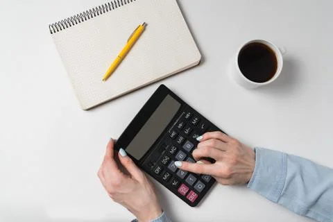 Flat lay. Women's hands and calculator near notebook and cup of coffee. White Stock Photos