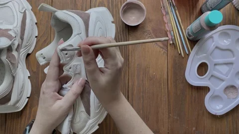 Flat lay of women's hands paint white boots with brush on wooden table. Stock Footage 181841544