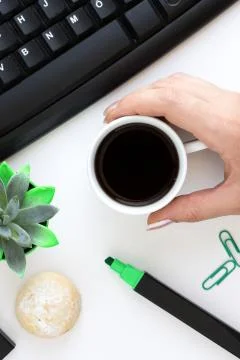 Flat lay workplace with a human hand holding cup of dark coffee Stock Photos