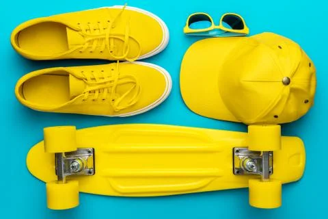 Flat lay of yellow baseball cap, sunglasses, sneakers, mini cruiser skateboard Stock Photos