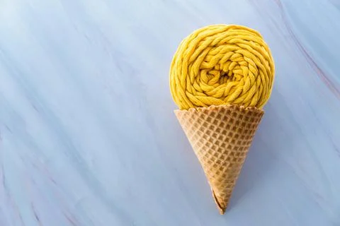 Flat lay of yellow macrame yarn skein in ice cream waffle cone on a marble Stock Photos