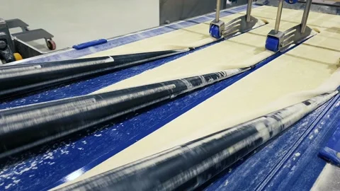 Flat layer of dough on moving conveyor belt prepared for making buns. Stock Footage 166575904