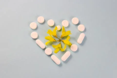 Flat mockup of white pills in the shape of a heart with yellow flowers in the Stock Photos