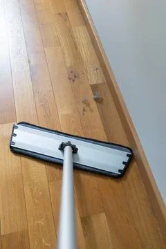 Flat mop positioned before accumulated dust along a baseboard Foto stock