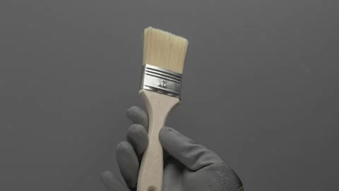A flat paint brush rotates in the hand on a gray background. Stockbeeldmateriaal 266893349