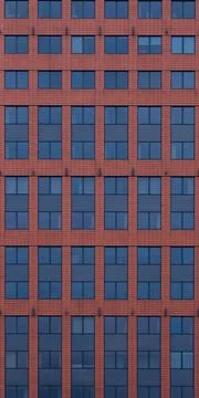 A flat red brick wall featuring windows with dark blue glass Foto stock