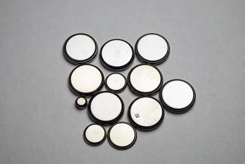 Flat round batteries of different sizes on a gray background Stock Photos