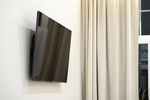 Flat screen television mounted on a plain white wall next to beige floor le.. Stock Photos