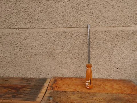 Flat screwdriver with orange handle standing on wooden table near rough wall, Photos