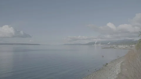 Flat sea with small rocky beach and paper mill chimney in distance Stock Footage 127041751