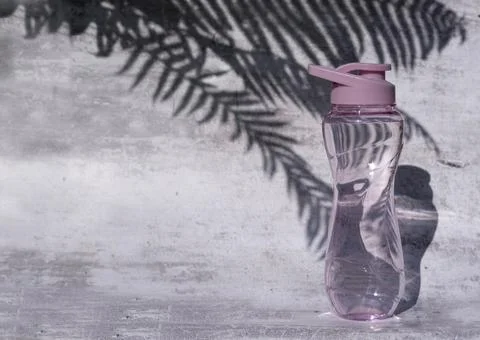 A flat shot of a plastic reusable bottle with an isotonic drink on a gray Stock Photos