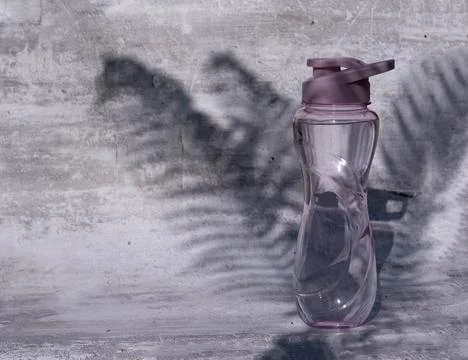 A flat shot of a plastic reusable bottle with an isotonic drink on a gray Stock Photos